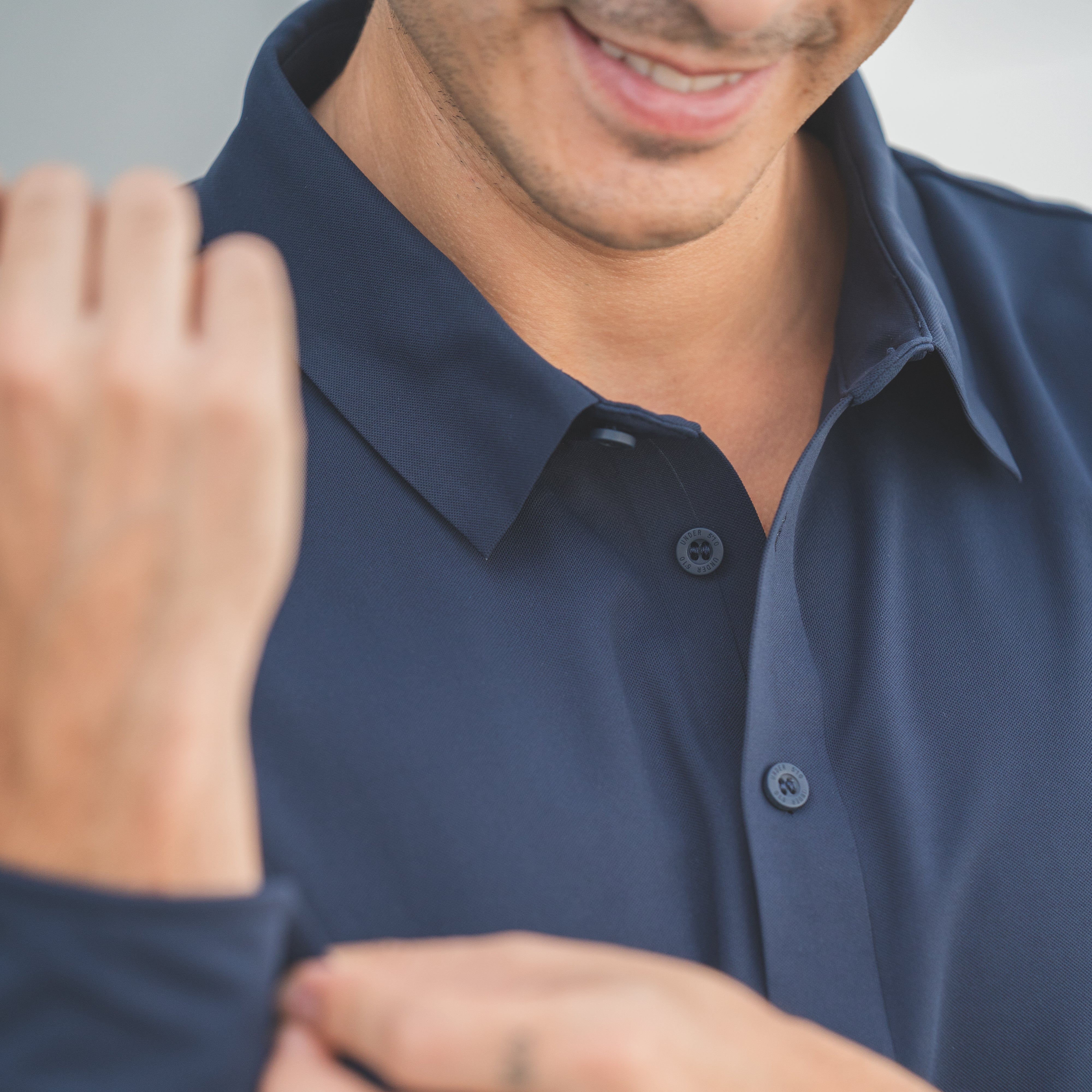 Man adjusting his navy blue shirt with a blurred background