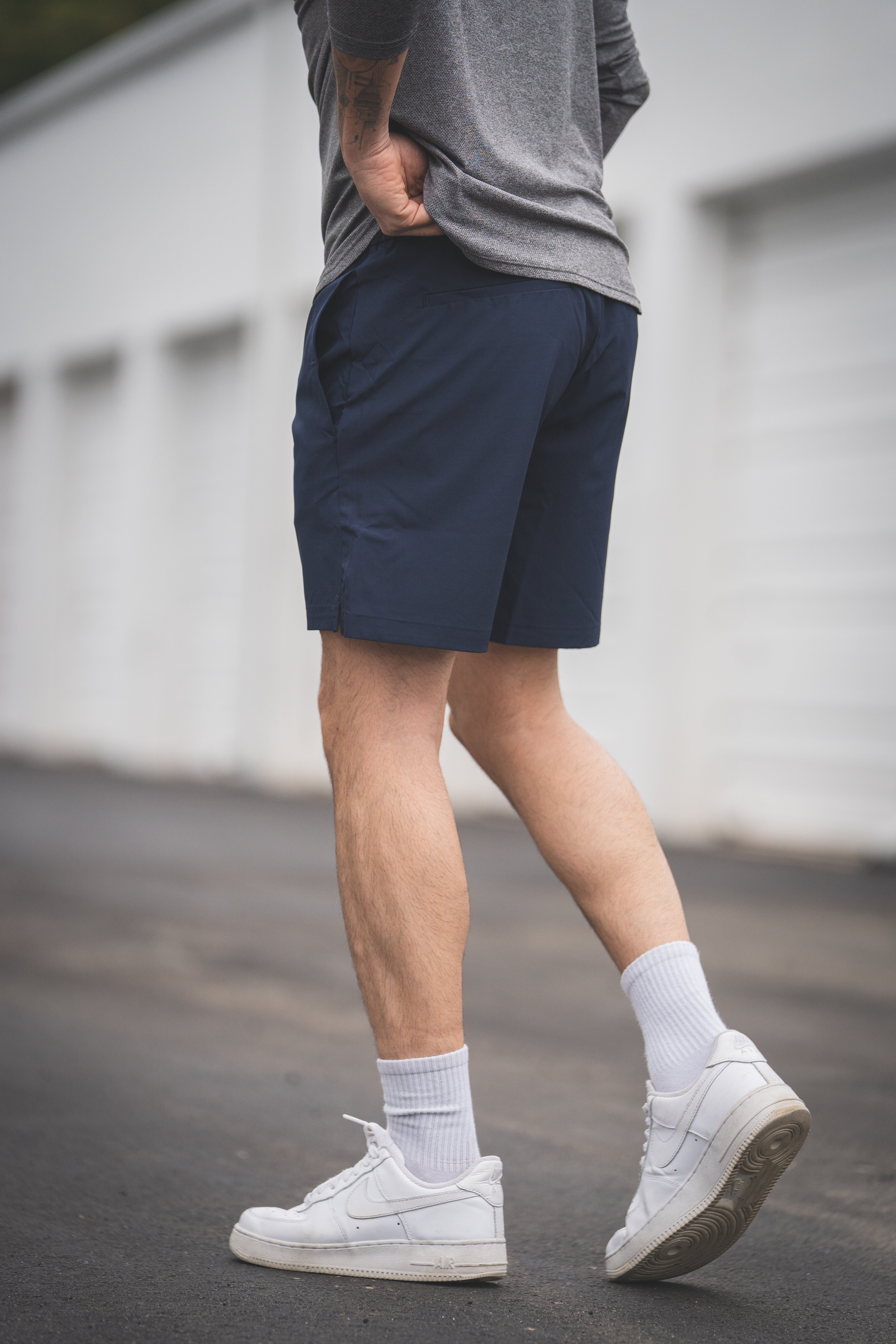 Person wearing navy shorts, gray shirt, white sneakers, and light socks on a blurred background