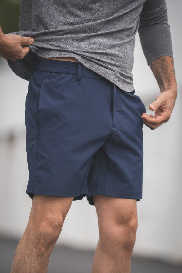 Person wearing navy shorts and a gray shirt against a blurred background