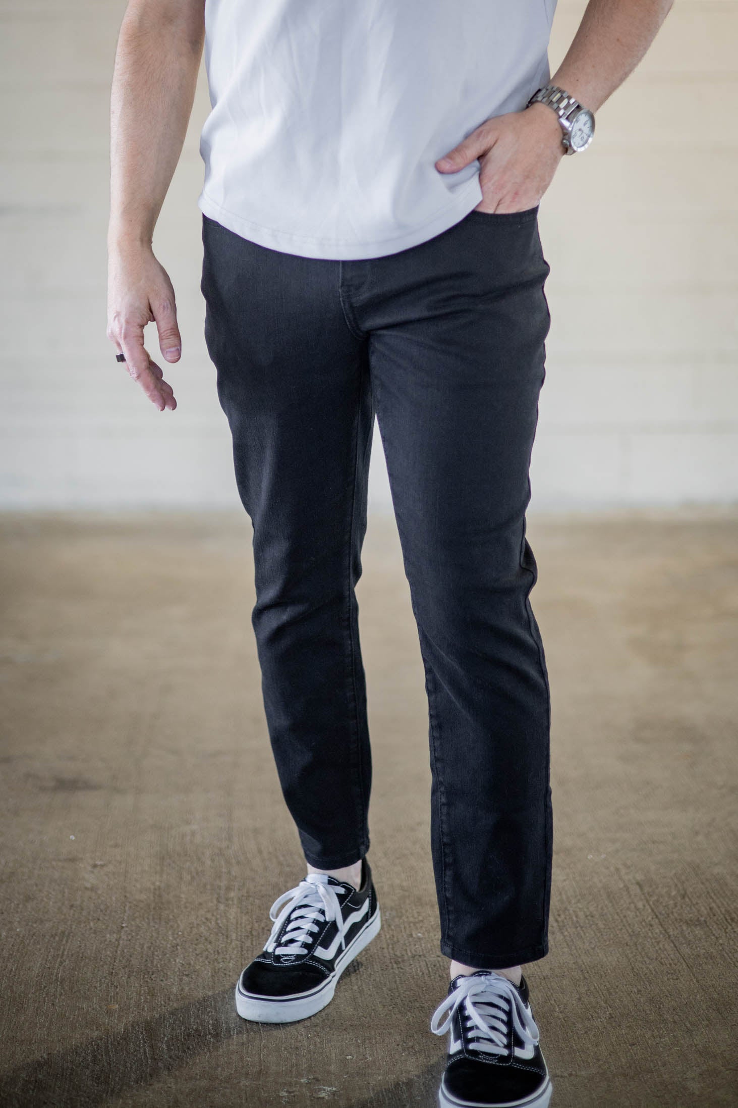 Male model wearing core extra stretch black jeans for short men with black canvas shoes with white shoelaces