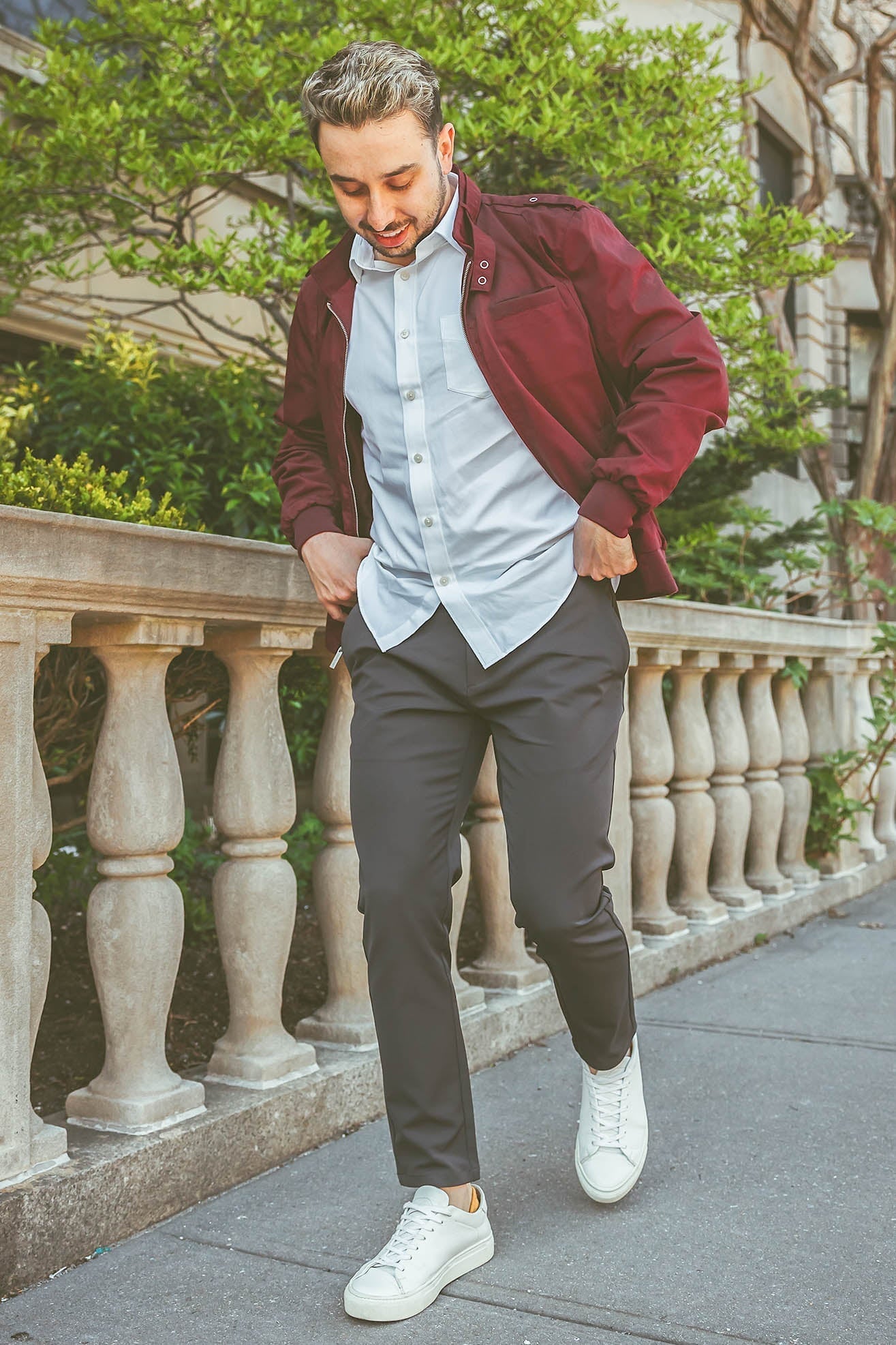 Male model wearing a red jacket with a button down shirt underneath, walking on sidewalk pulling charcoal super stretch performance pants up from under510.com